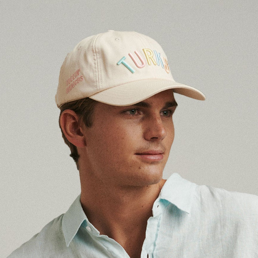 A person wearing a beige 'OKAICOS' branded cap with embroidered details.