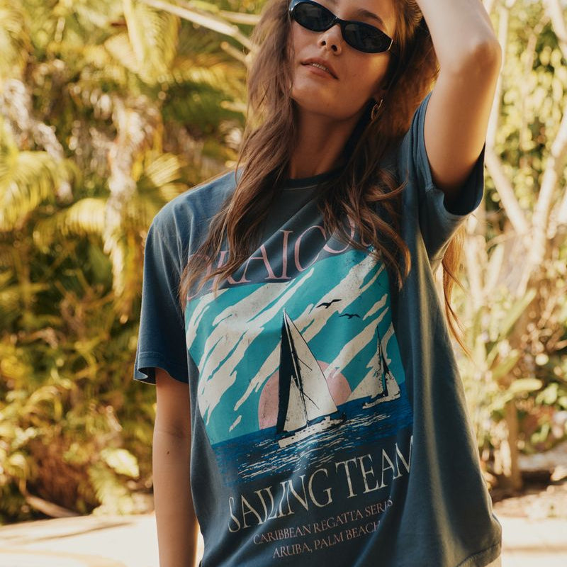 Woman wearing an Okaicos 'Sailing Team' t-shirt with a sailboat design outdoors.