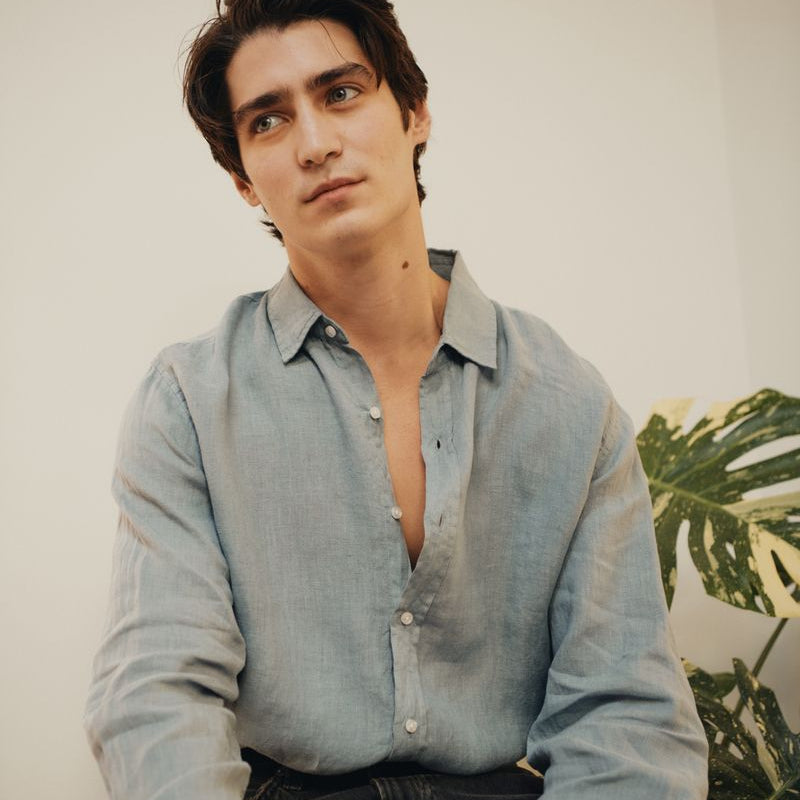 Man wearing a slate grey linen shirt with a plant in the background