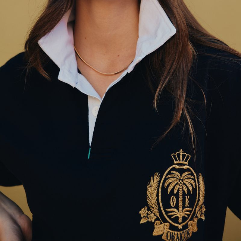 Woman wearing a black polo shirt with a gold emblem and white collar against a yellow background