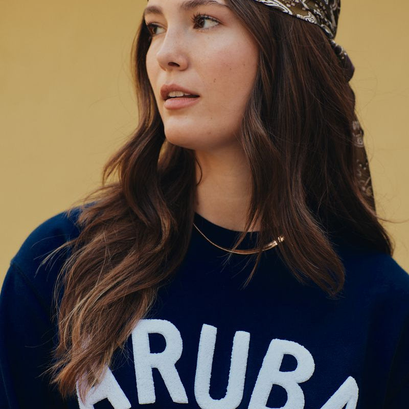 Woman wearing a headscarf with 'ARUBA' text on a dark background