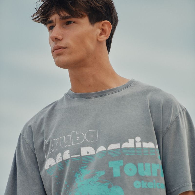 Man wearing a gray t-shirt with teal and white text and graphics