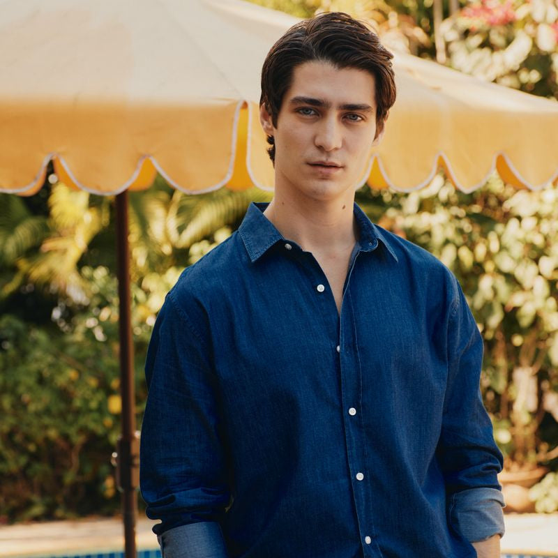 Man in a blue shirt standing under a yellow umbrella by a pool