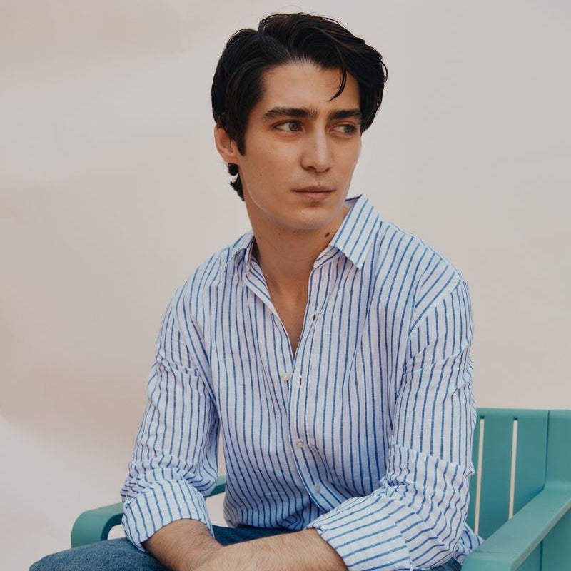 Man sitting on a green chair wearing a blue and white striped shirt and jeans.