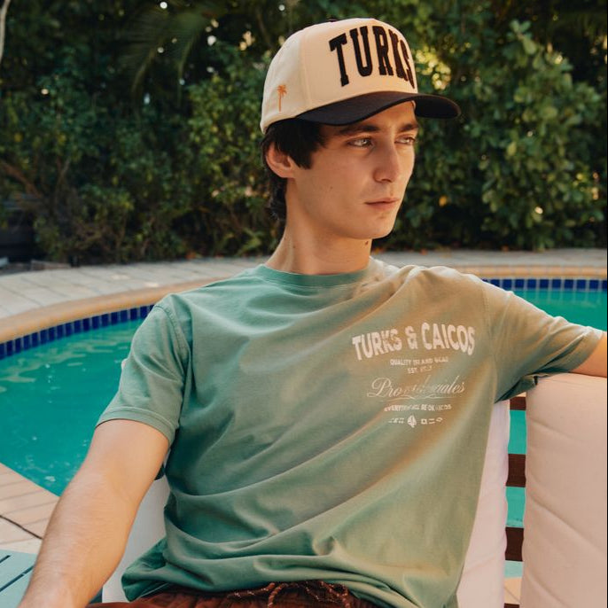 Person wearing an Okaicos cap and t-shirt by a poolside