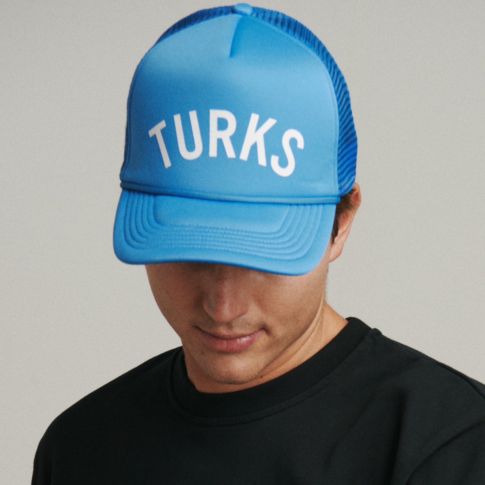 A person wearing a royal blue trucker hat with the word 'TURKS' printed on the front.