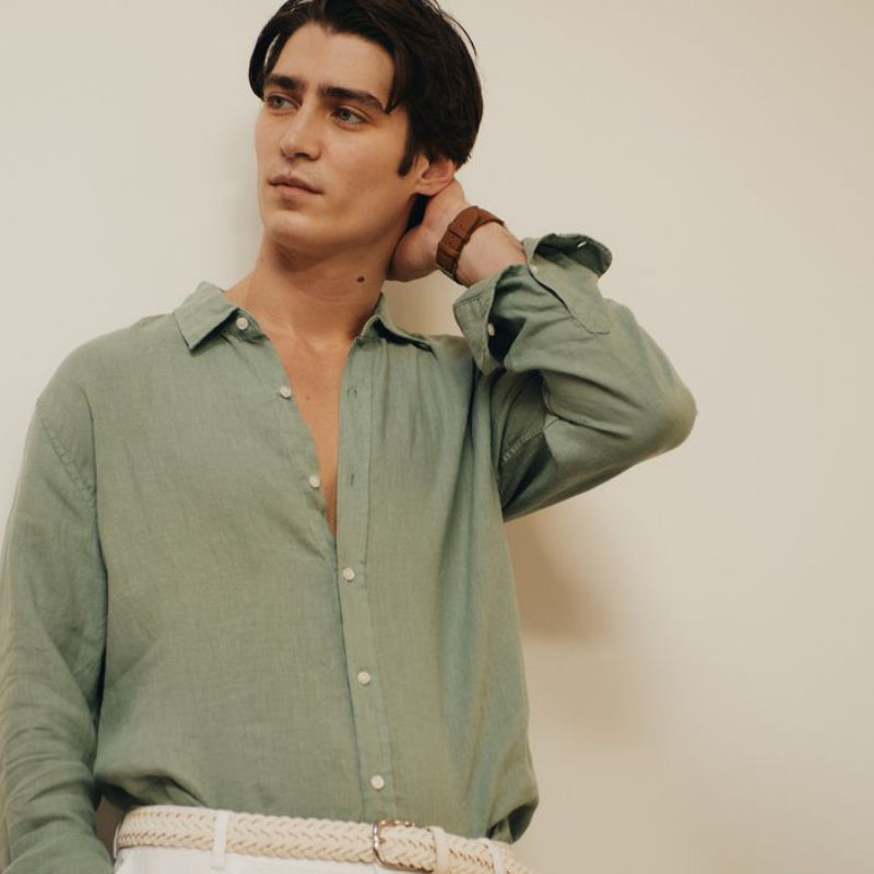 Man wearing a light green okaicos shirt and white pants against a plain background