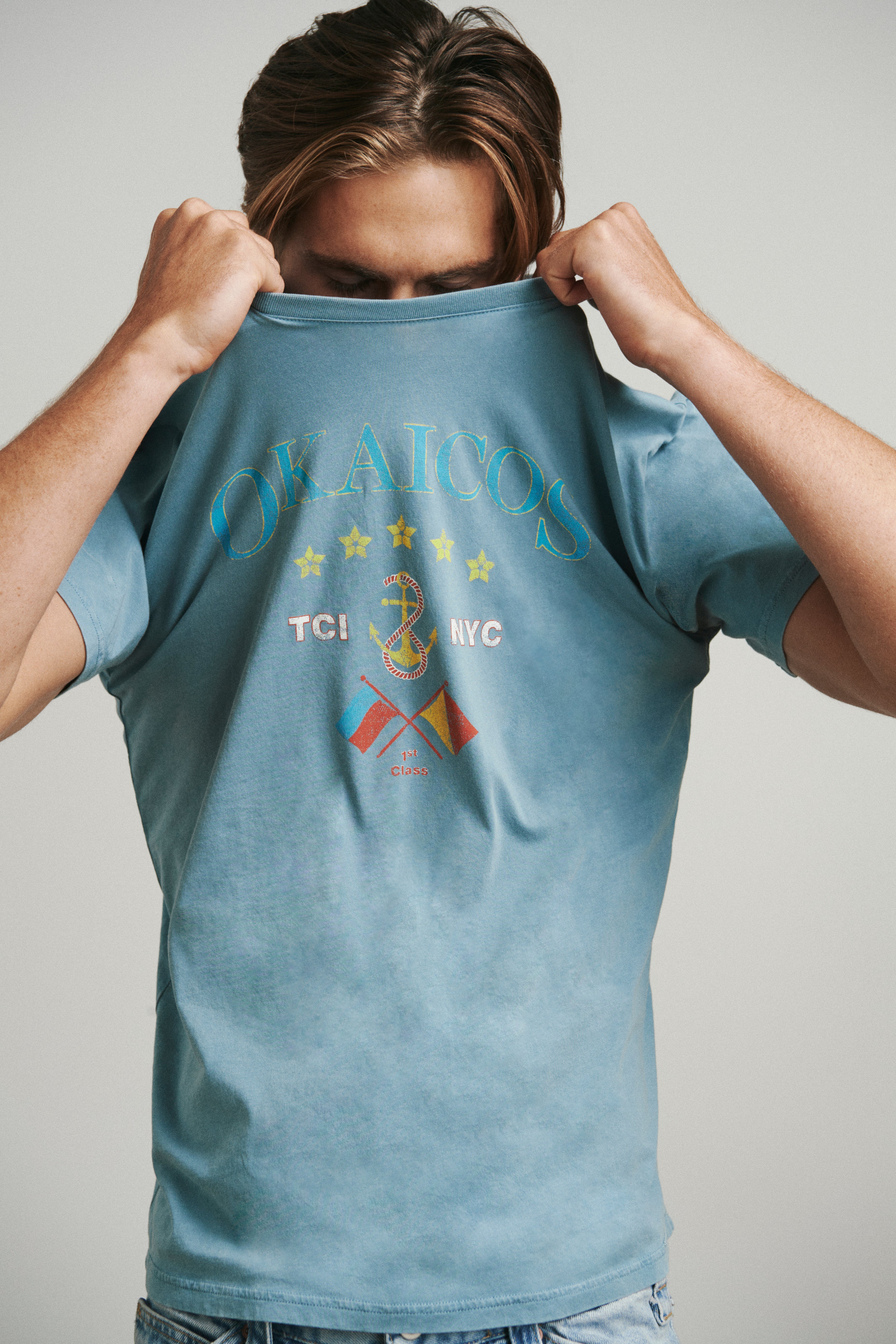 Person wearing a blue t-shirt with graphics and text on a plain background