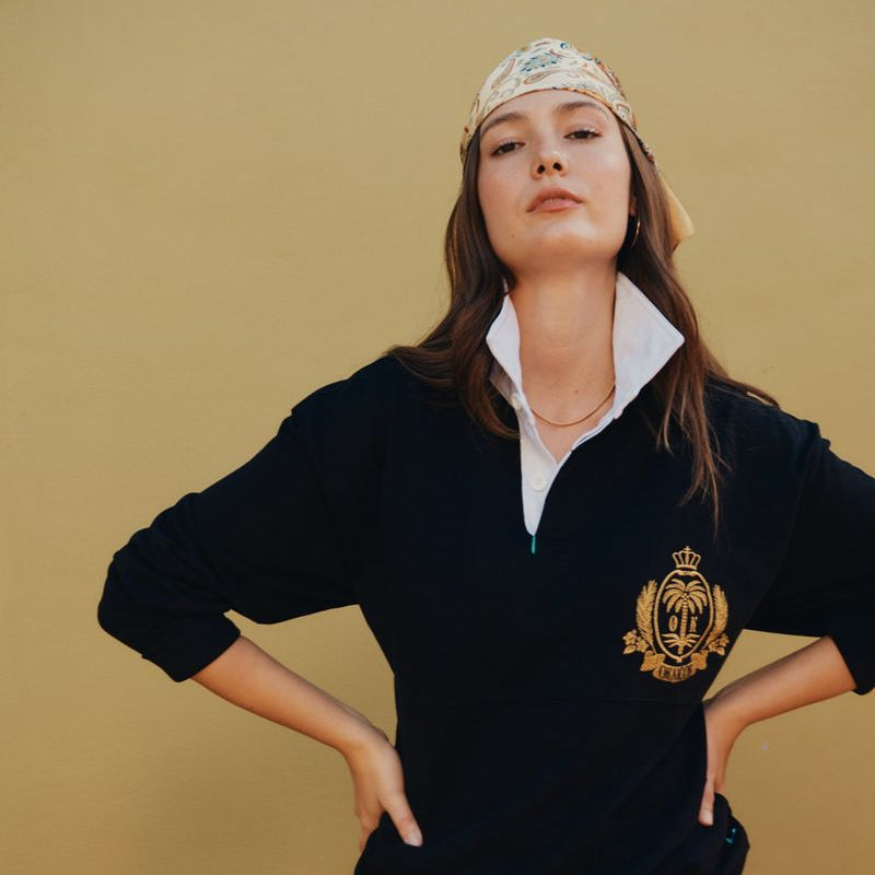 Person wearing a black sweater with a logo and shorts against a beige background