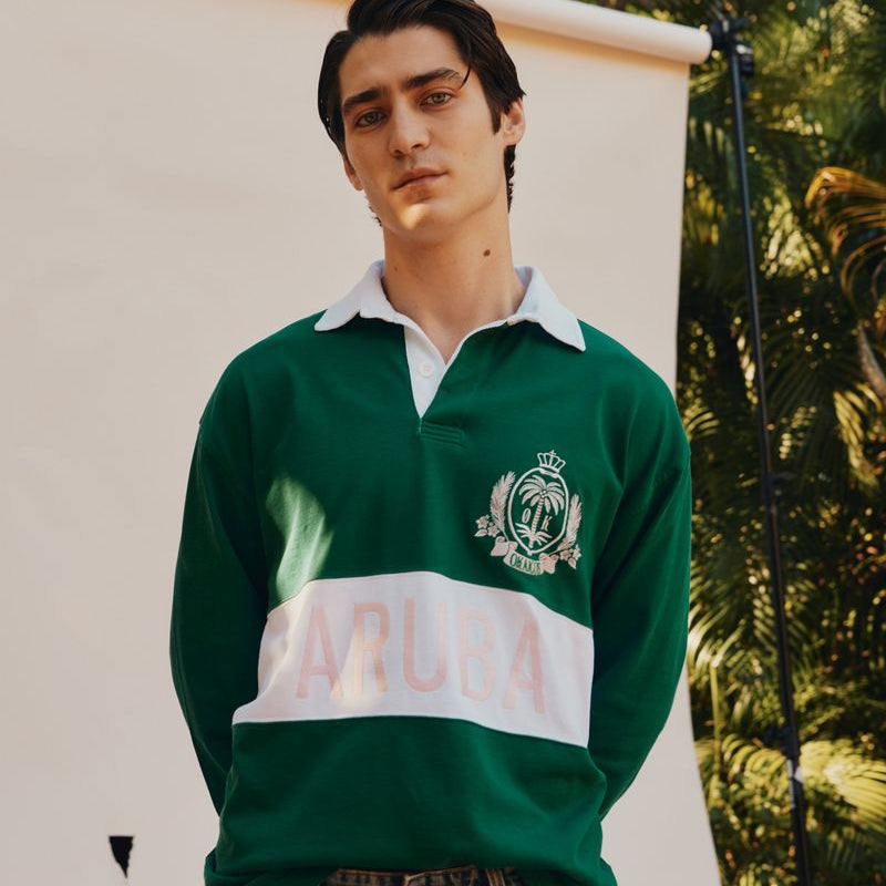 Man wearing a green and white rugby shirt with a logo, standing outdoors.