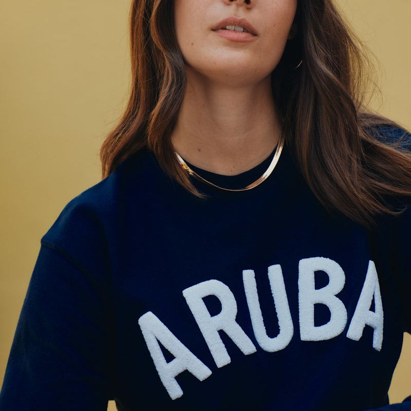 Person wearing a navy blue sweatshirt with 'ARUBA' printed on it against a yellow background