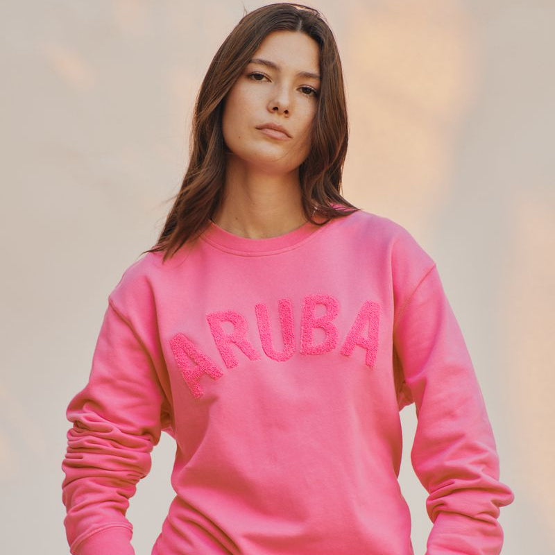 Person wearing a pink sweatshirt with 'ARUBA' text against a blurred background
