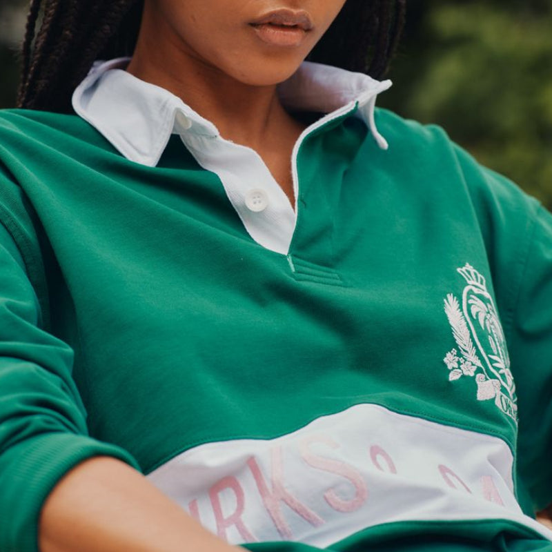 Person wearing a green sports jersey with a logo and text, sitting outdoors.