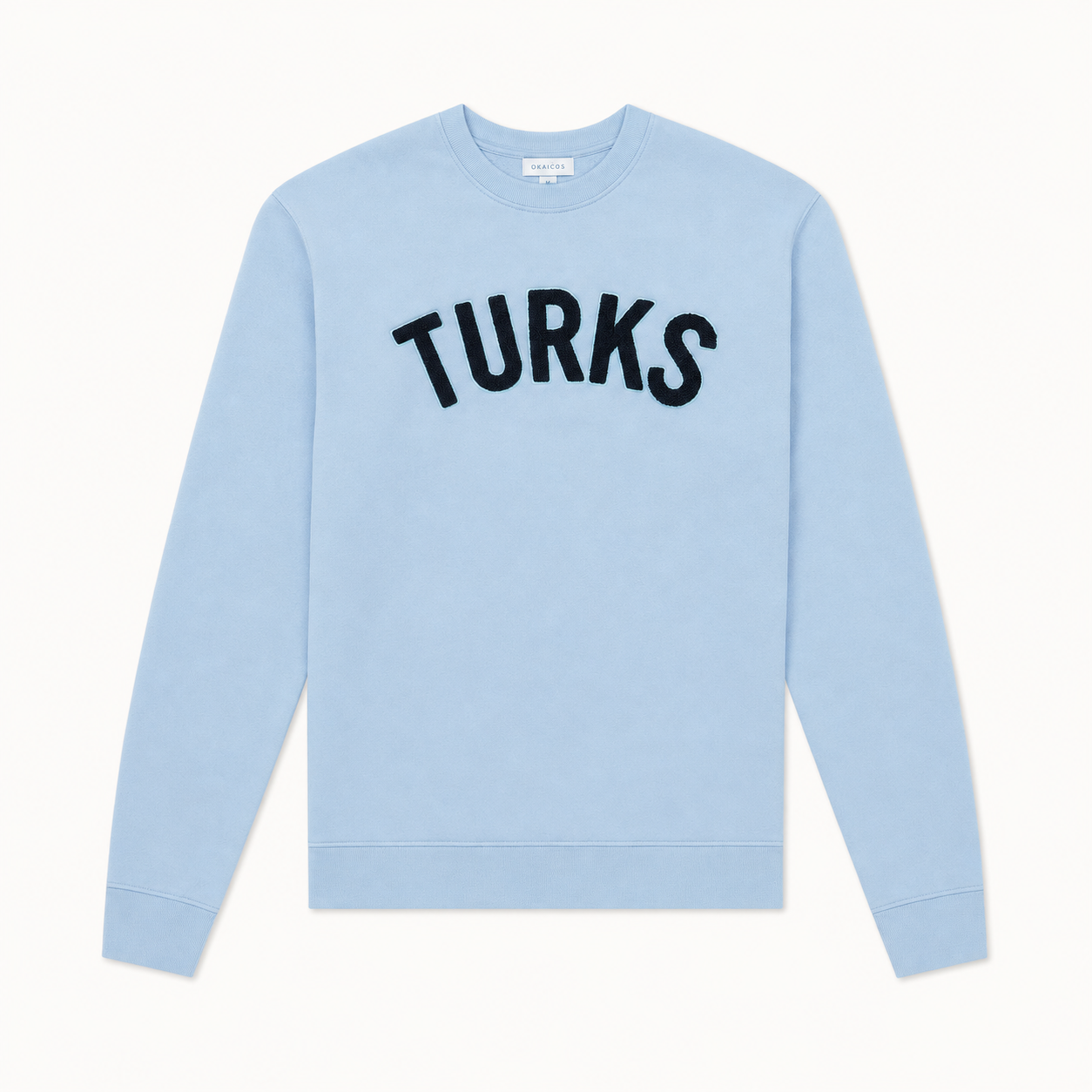A light blue crewneck sweatshirt with the word 'TURKS' printed in black arched letters across the chest, displayed flat against a light off-white background.